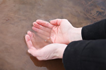 A woman's hands scooping water from a pond.
