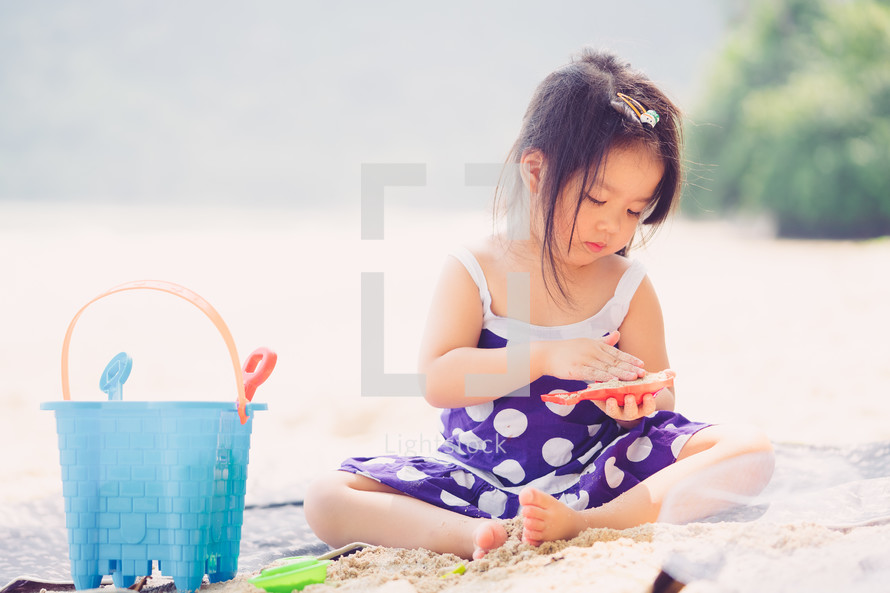 a girl on a beach playing with sand toys 