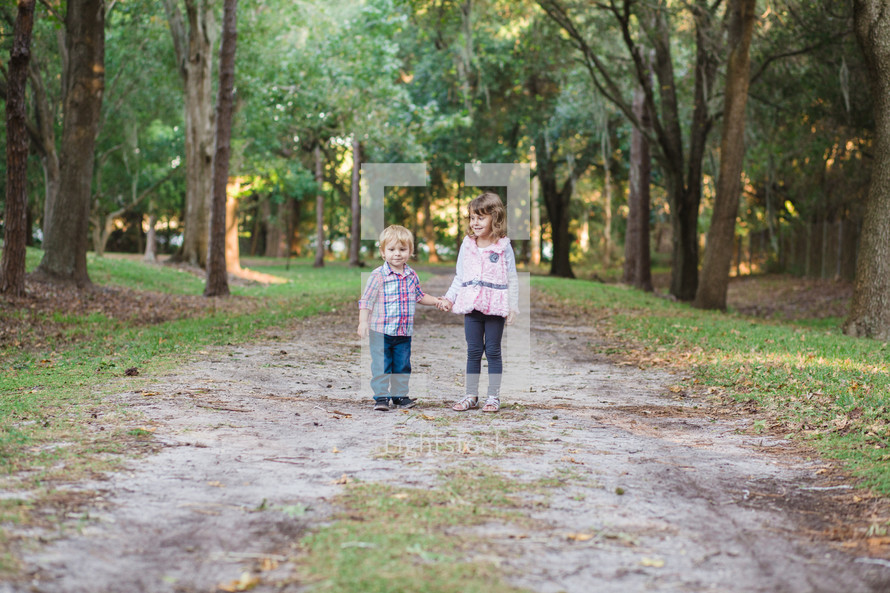 brother and sister walking on a dirt road 
