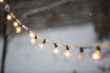 falling snow and a string of glowing lightbulbs