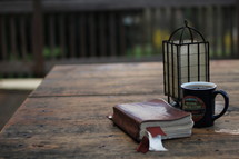 Bible, coffee mug, and lantern on picnic table 