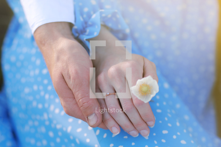 romantic date concept. young man and woman hands holding each other. girl with golden ring on finger in blue dress with chamomile flower in hand.