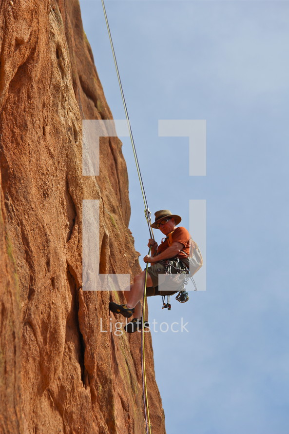 Man rappelling down a steep rock face after climbing mountain 