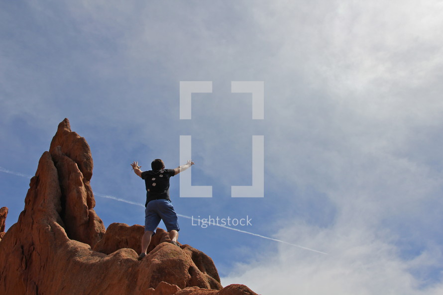 man with his hands raised in the air in victory and accomplishment standing on top of a mountain 