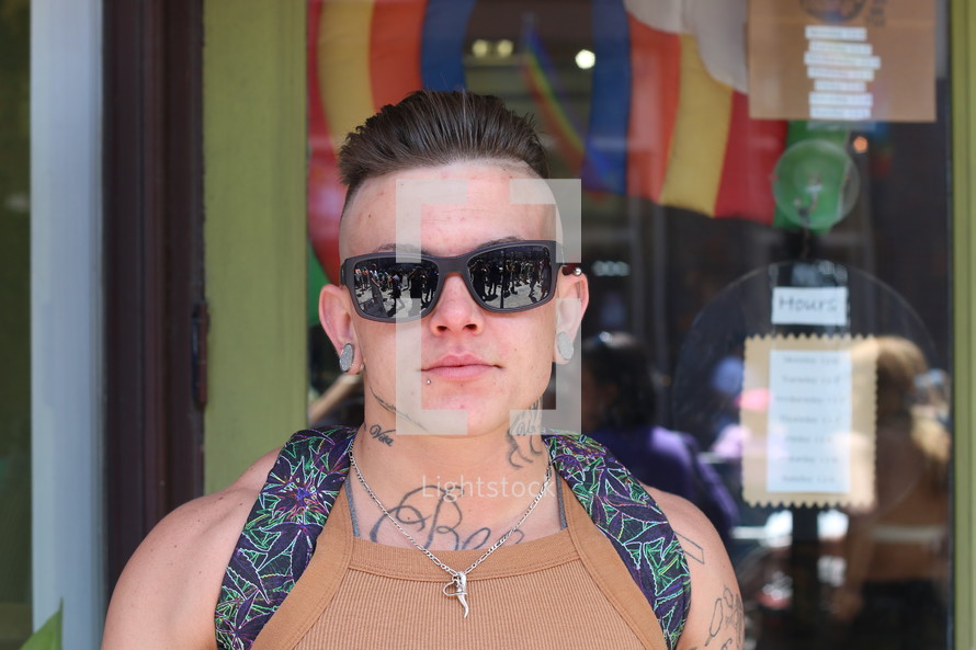 man with sunglasses, tattoos, ear gauges, and a backpack 
