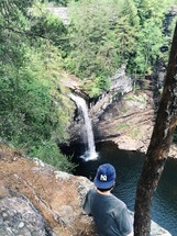 man standing at the edge of a cliff looking down at a waterfall 