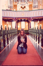 woman kneeling in an aisle of a church in prayer 