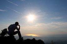 Silhouette of a man in thought / prayer sitting on a mountain top 