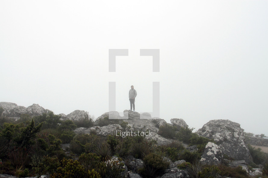 a man standing on rocks in the fog 