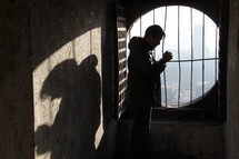man standing in prayer in front of a barred window