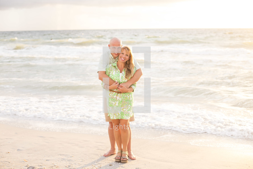husband and wife hugging on a beach 