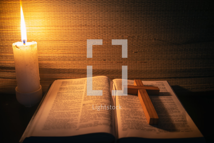 candle light with holy bible and cross on wooden table in the night time.