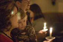 father, mother and child holding candles at a Christmas Eve church service