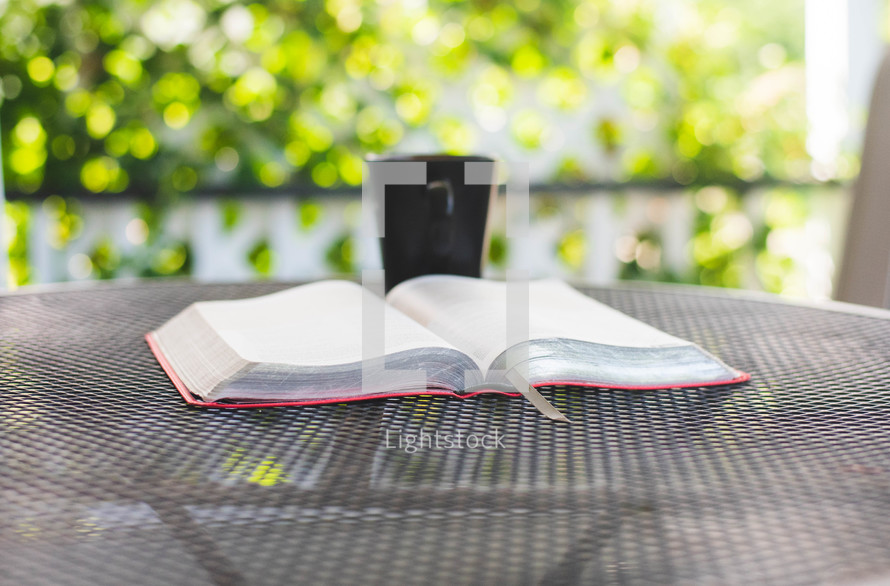 a opened Bible and coffee cup on an outdoor table 