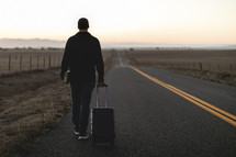 a man walking down a road carrying luggage 
