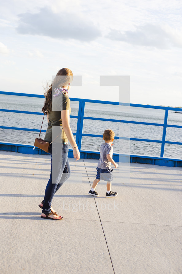 a mother and son walking on a harbor sidewalk 