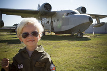 a boy child in a fighter pilot outfit in front of a bomber