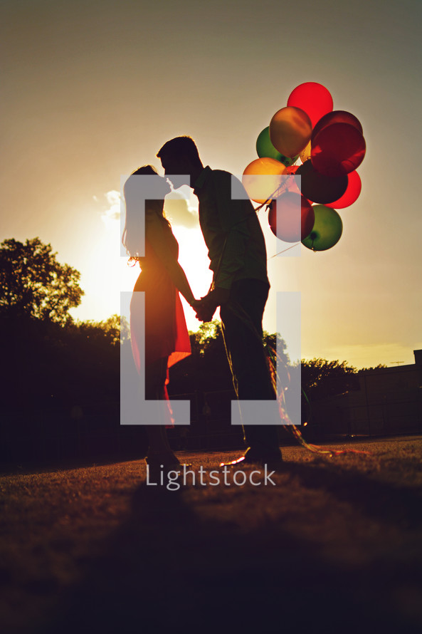 couple holding balloons at sunset 