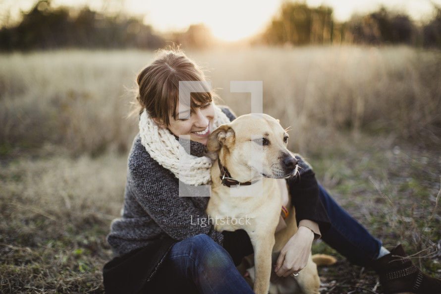 Smiling woman witting with her dog in a field.