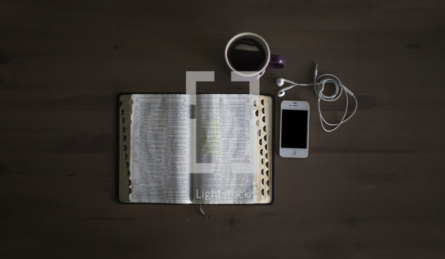 An open Bible, cup of coffee and cell phone on a table.