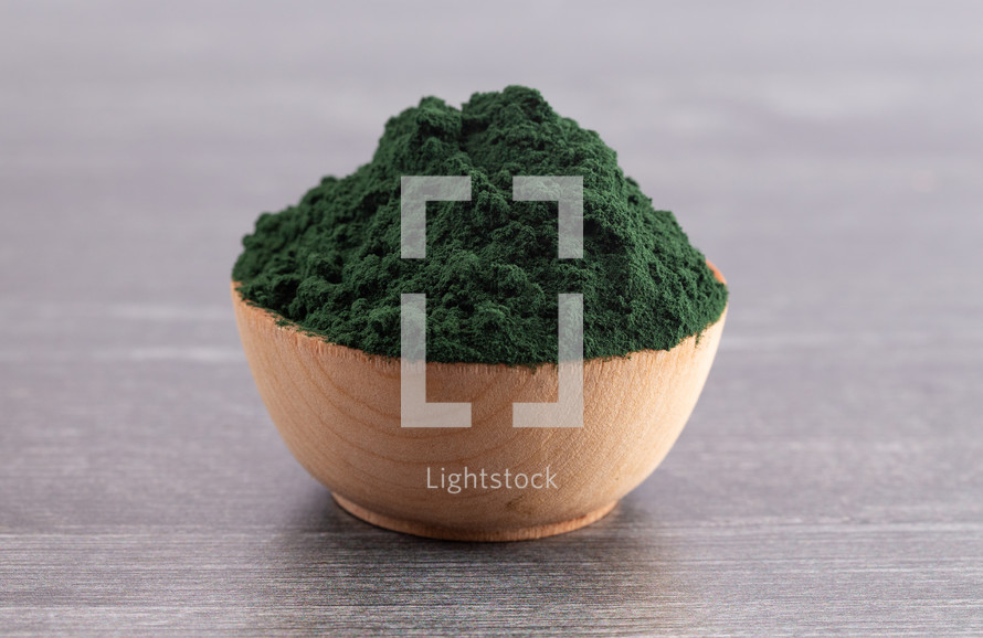 A Wooden Bowl Full of Spirulina Powder on a Wood Background