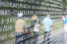 Reflection of people in the Vietnam Memorial wall where names are carved.