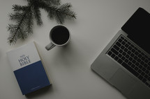A Bible, computer, and cup of coffee on a white surface.