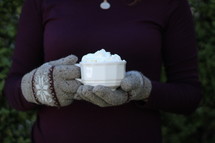a woman in gloves holding a mug of hot cocoa 