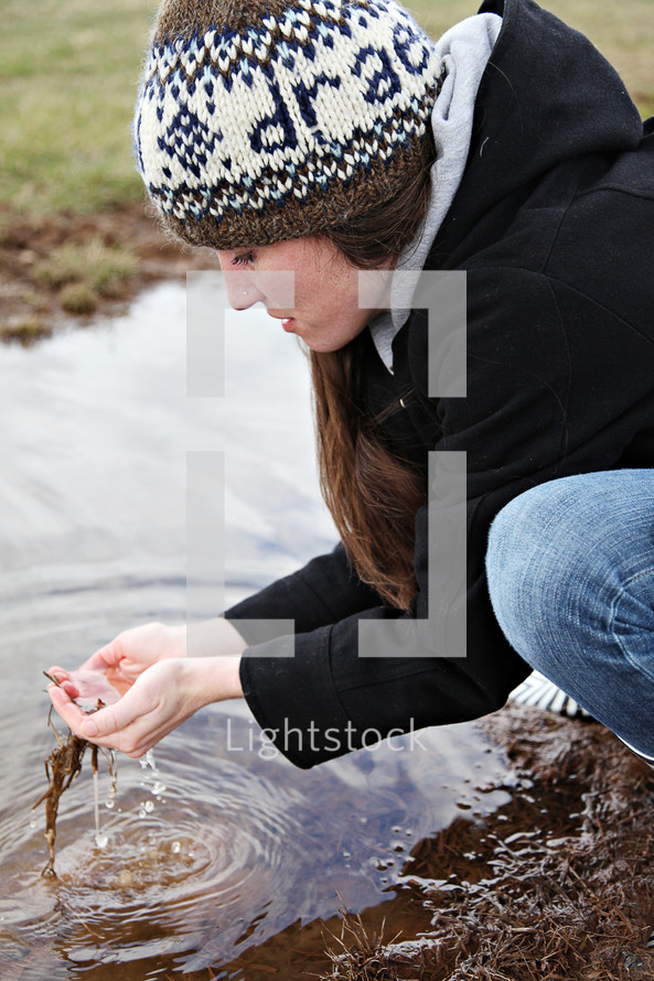 A woman scooping water in her hands from a stream.