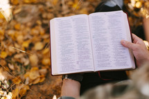 reading a bible standing in fall leaves 