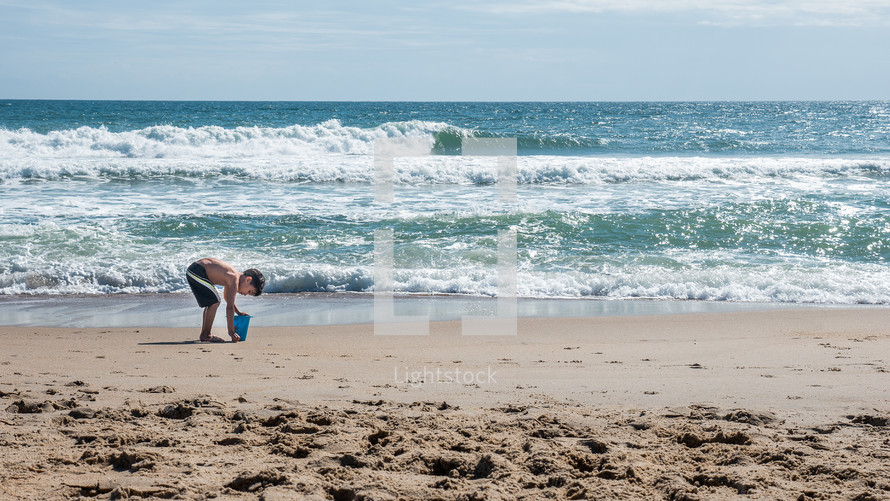 child playing with a sand bucket on a beach 