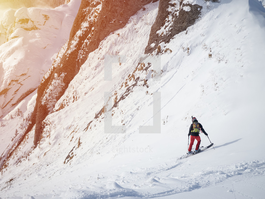 Lonely free-rider skier in high mountains. Extreme freestyle skiing in sunny daylight on winter mountain landscape