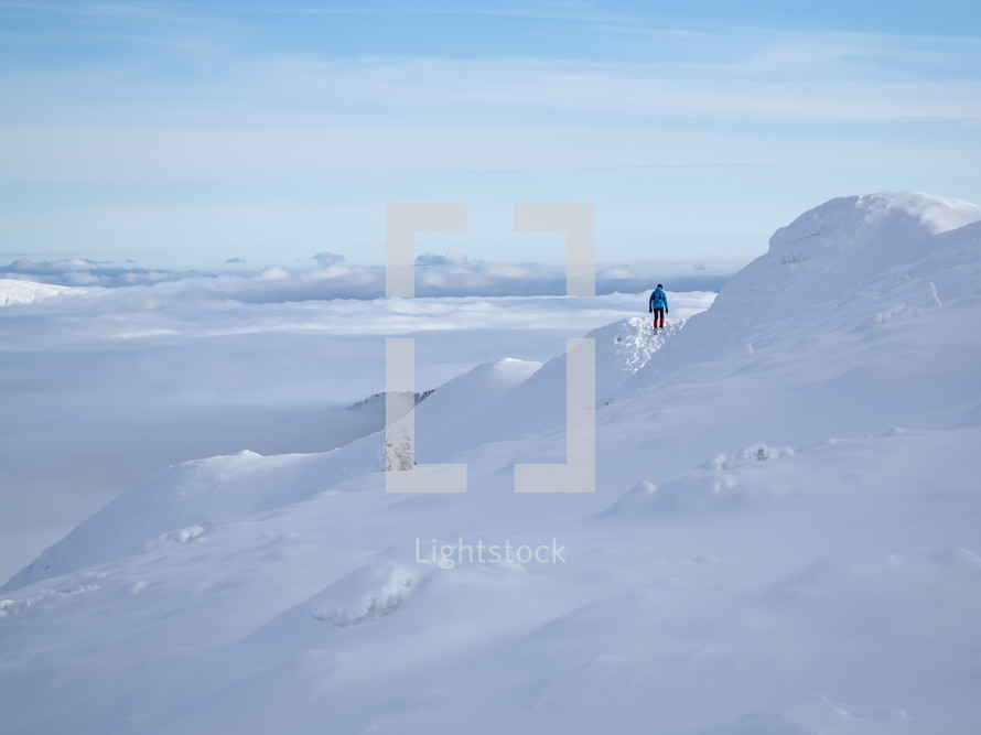 Man with backpack hiking on a mountain track above clouds in sunny day, Winter season with snow on mountain