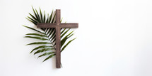 Palm Sunday. Wooden christian cross with palm leaf on white wall background.