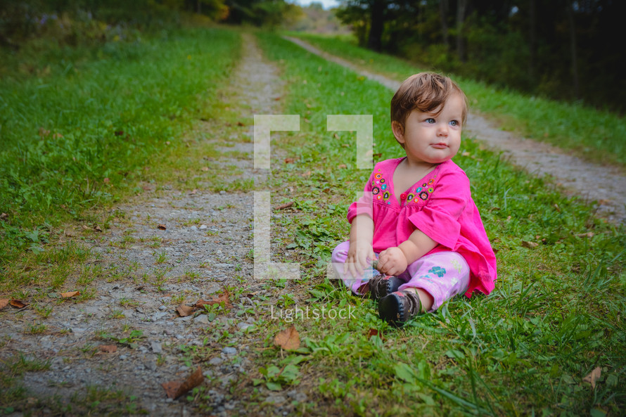 infant girl sitting on a country road 