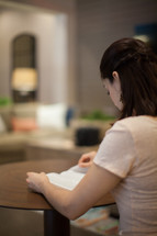 A young woman sitting at a table reading the Bible