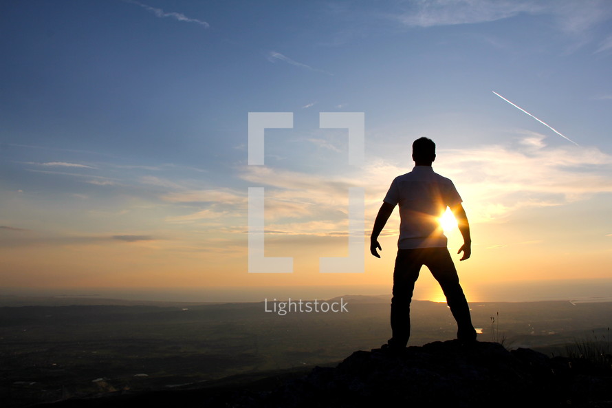 silhouette of a man standing on a mountain top at sunset / sunrise