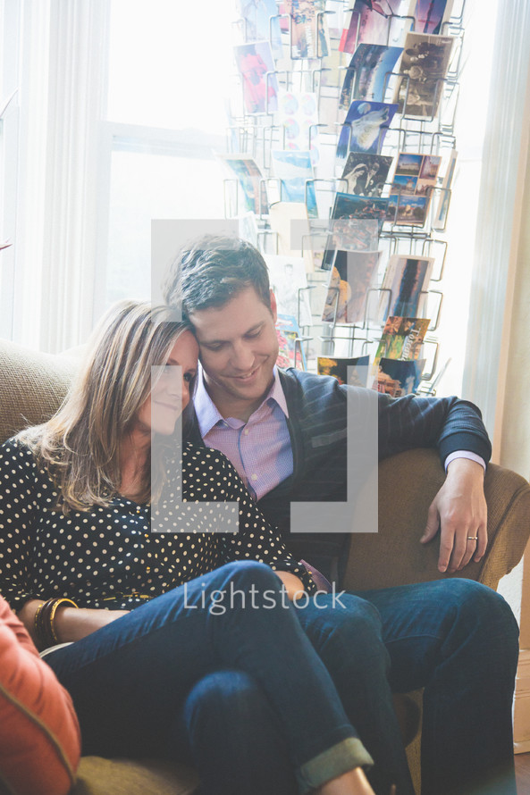 Smiling and embracing couple sitting on a sofa near a rack of postcards.