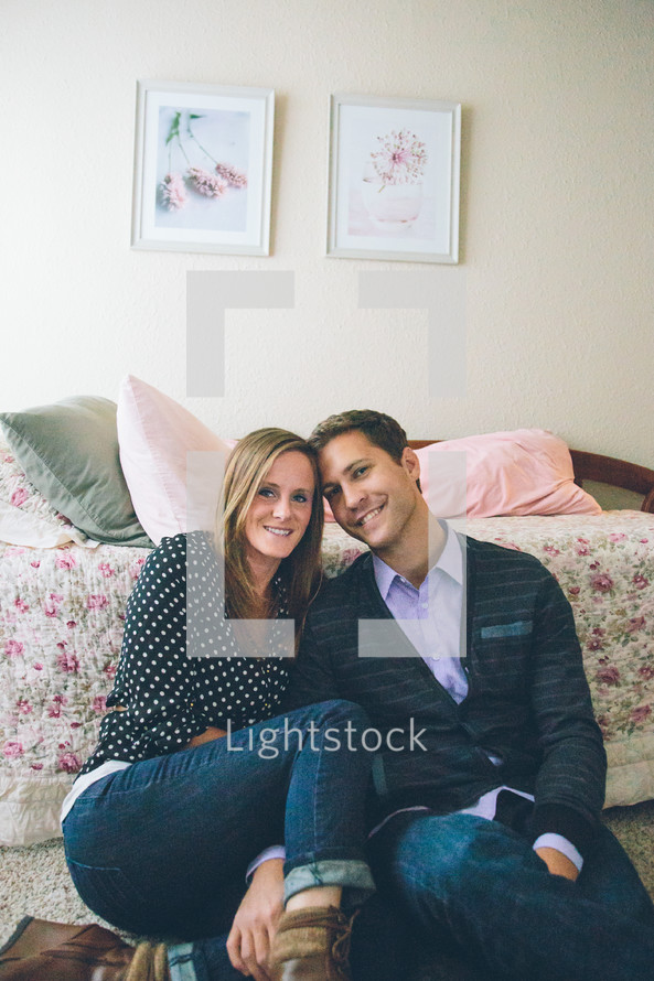 A man and woman sitting closely together next to a bed.