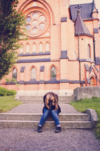 woman with her head down sitting in front of a church 