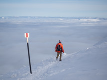 Man with backpack hiking on a mountain track above clouds in sunny day, Winter season with snow on mountain.