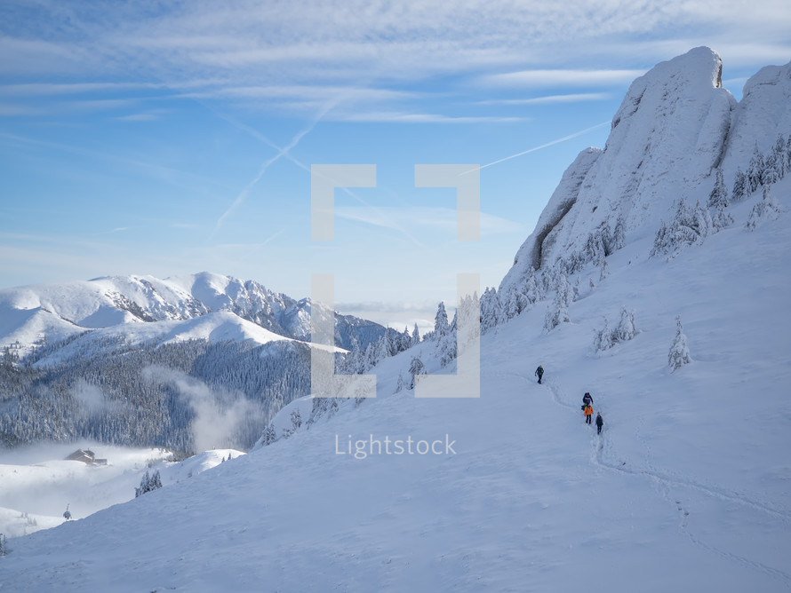 Mountain hikers on a path in snow to moutain summit, in a bright sunny winter day. Winter outdoor activity