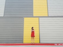 woman in a red dress standing in front of a yellow and gray wall 