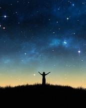woman standing with her arms raised in worship under stars in the night sky