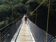 A hiker walks across a suspension bridge.