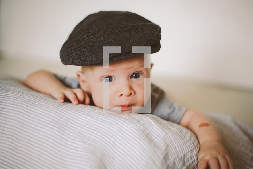 Infant boy in a hat propped up on a pillow.
