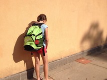 a girl child with a book bag looking down 