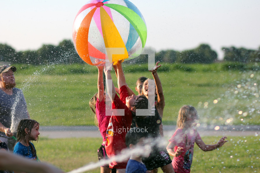 children playing outdoors with beach balls and water hoses 