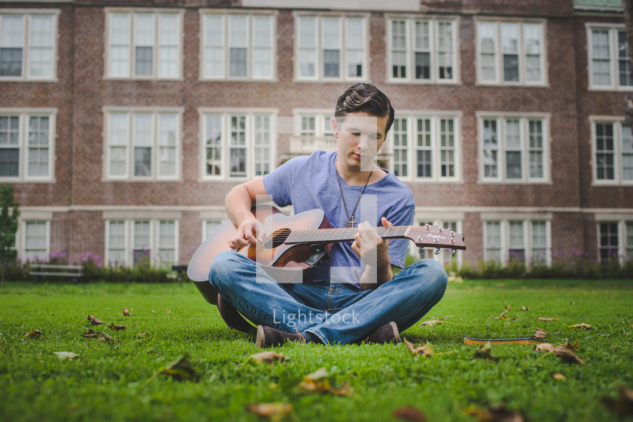 man sitting in grass playing a guitar 