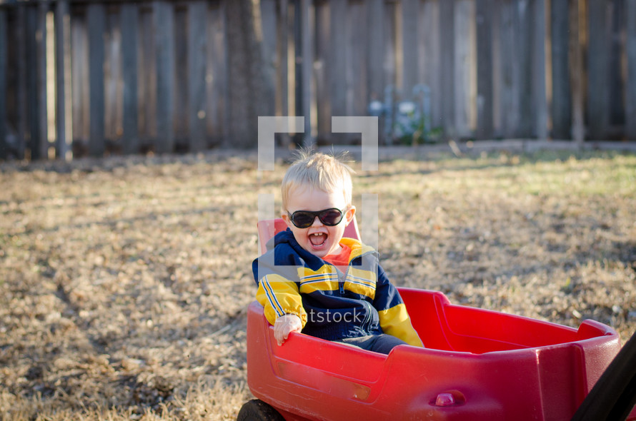 a happy toddler boy in a red wagon 
